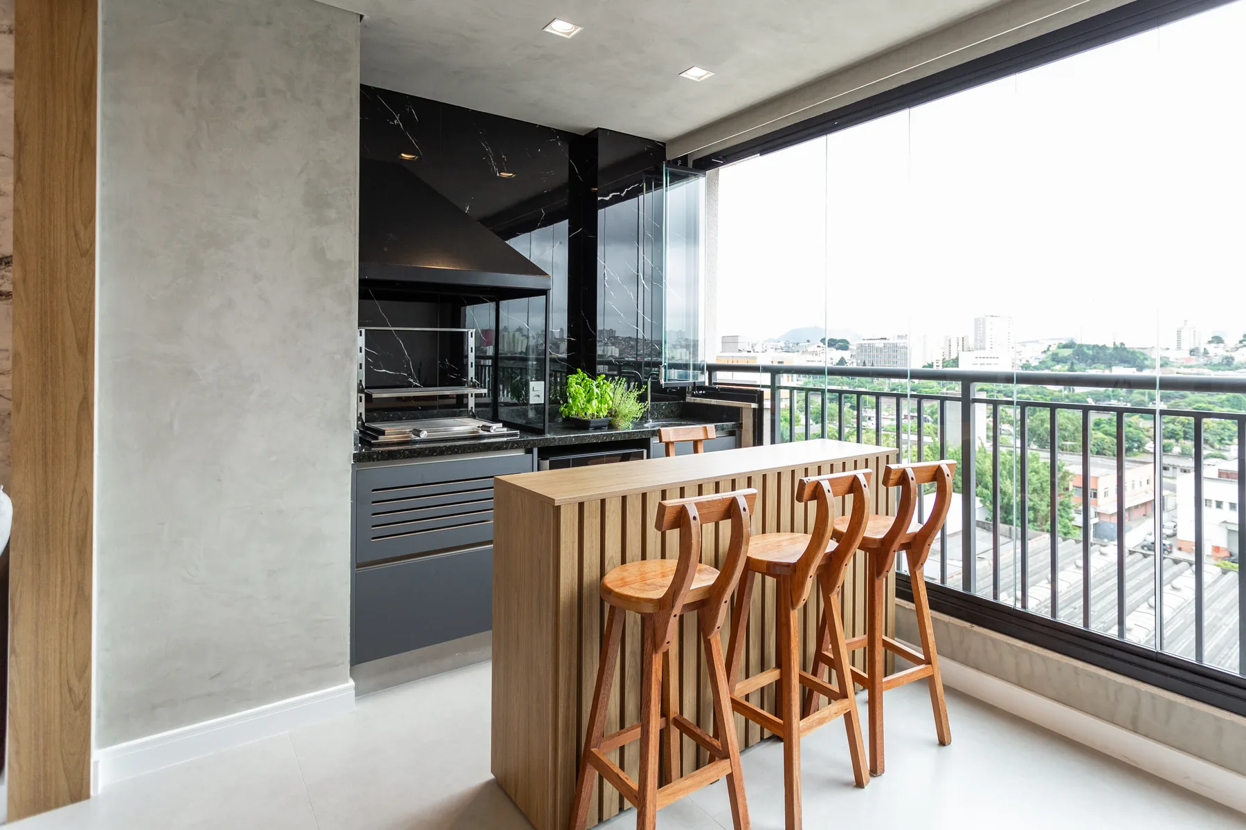 Área gourmet planejada com revestimento em mármore preto, marcenaria em madeira clara e churrasqueira, projeto Linear em apartamento no ABC Paulista
