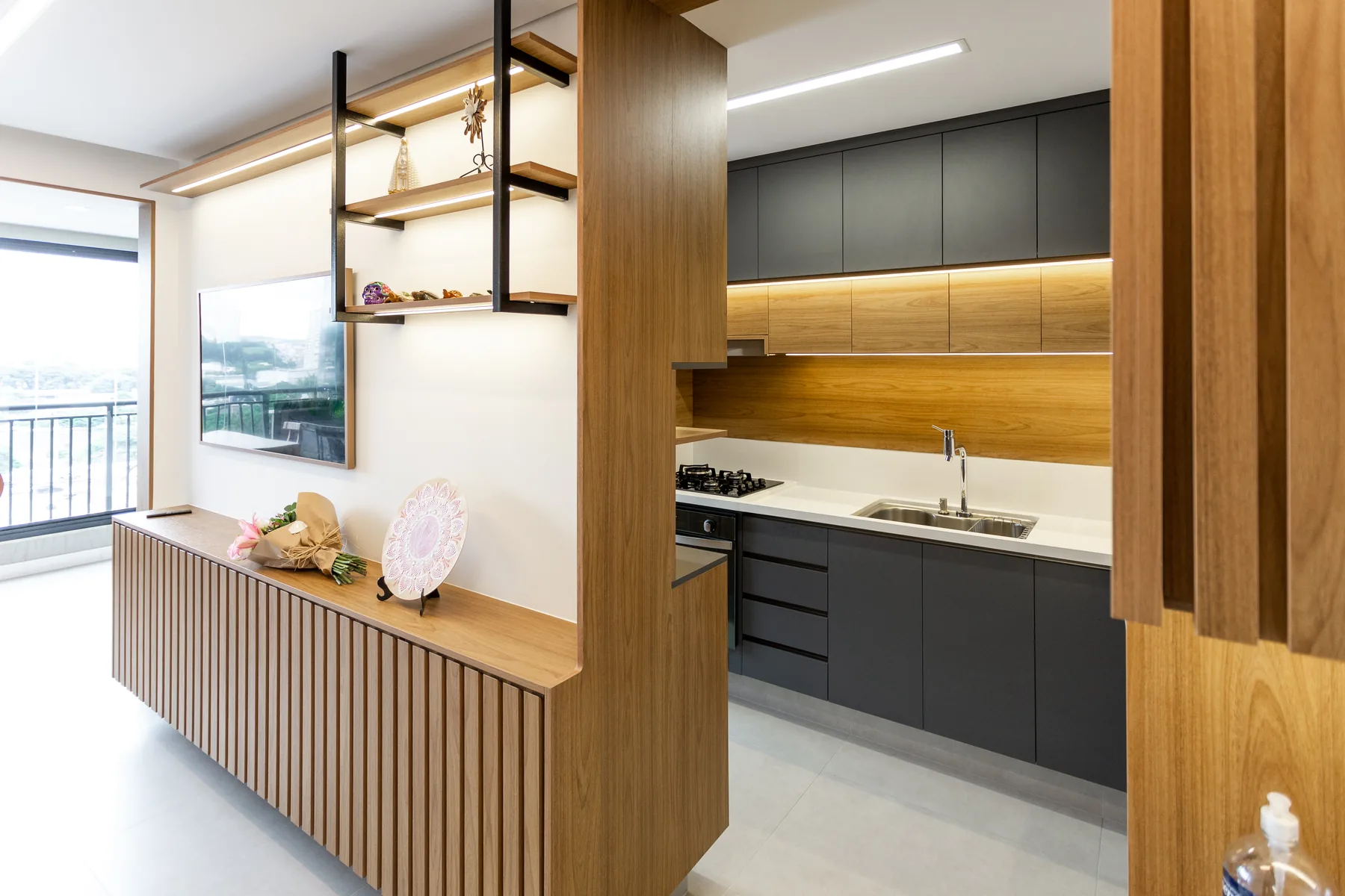 Cozinha americana planejada integrada com a sala, com aparador ripado de madeira e prateleiras iluminadas, projeto Linear em São Paulo