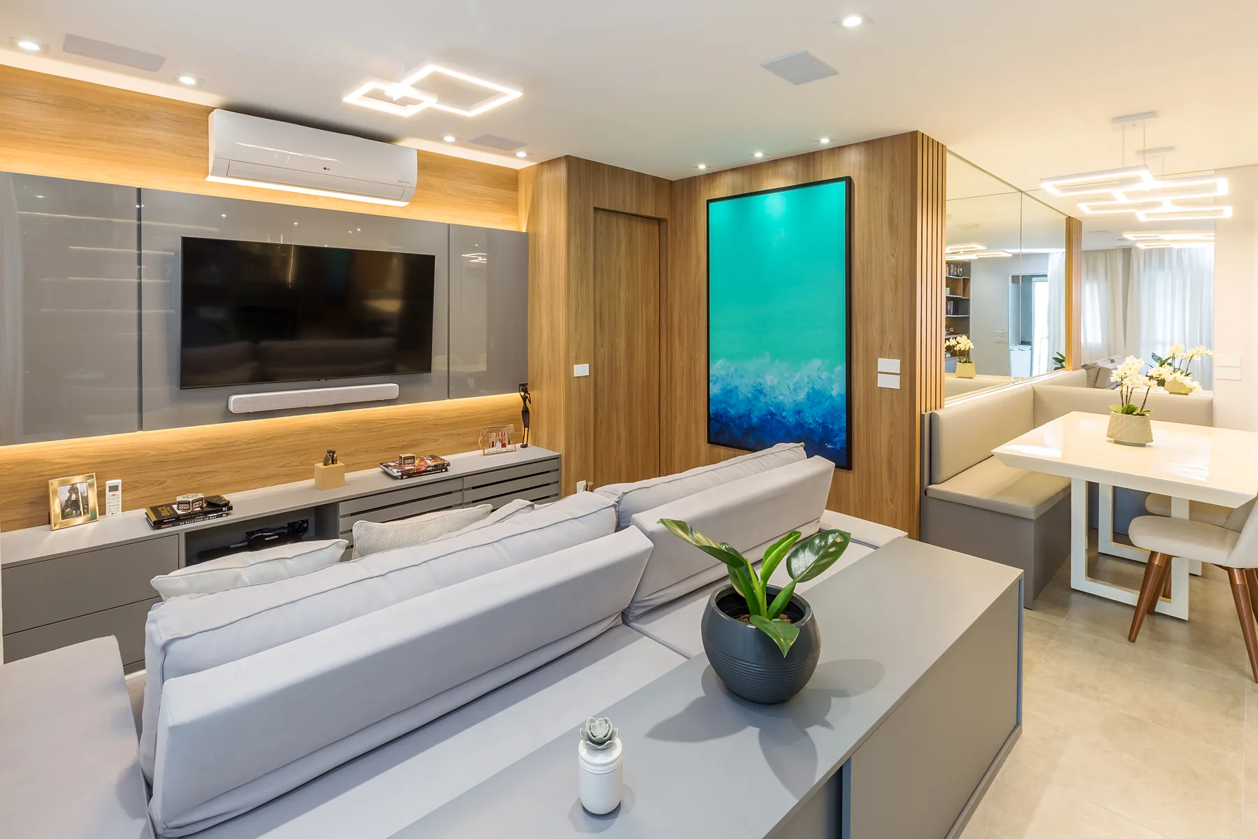 Sala de estar planejada com painel de TV em laca branca, madeira ripada iluminada e espelho lateral, projeto Linear em São Paulo